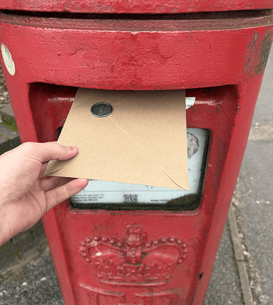 A wax-sealed Rewild bamboo letter being posted in a Royal Mail postbox